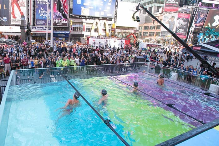swimmers inside a glass pool on side city street